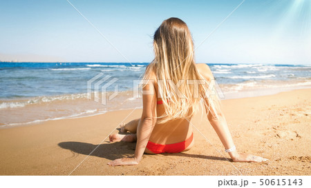 Sexy young woman with long hair wearing red bikini sitting on the beach 50615143