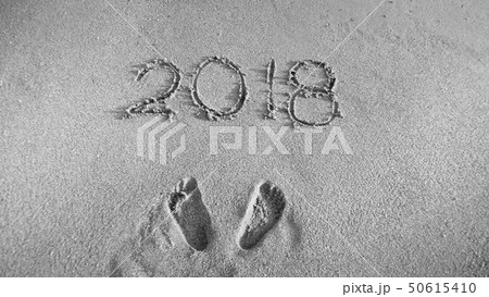 Black and white image of footprints and 2018 numbers written on sand beach. Concept of celebrating Black and white image of footprints and 2018 numbers written on sand beach. Concept of celebrating 50615410