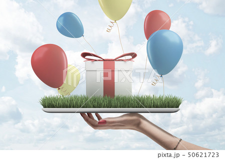 Side view of woman's hand holding digital tablet with green grass on screen, gift box standing on Side view of woman's hand holding digital tablet with green grass on screen, gift box standing on 50621723