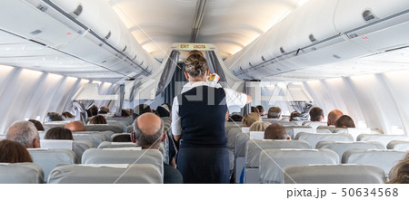 Interior of commercial airplane with stewardess serving passengers on seats during flight. 50634568