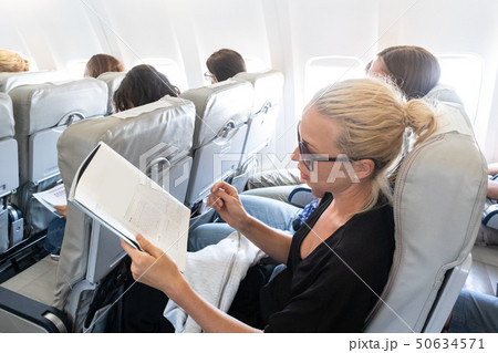 Woman reading magazine on airplane during flight. Female traveler reading seated in passanger cabin. Woman reading magazine on airplane during flight. Female traveler reading seated in passanger cabin. 50634571