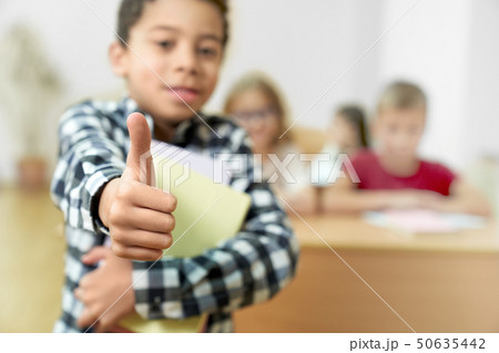 Schoolboy standing in class showing thumb up. 50635442
