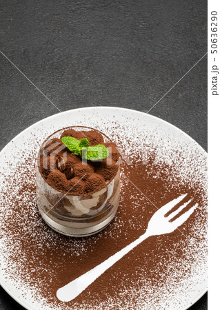 Classic tiramisu dessert in a glass on plate with fork silhouette on dark concrete background Classic tiramisu dessert in a glass on plate with fork silhouette on dark concrete background 50636290
