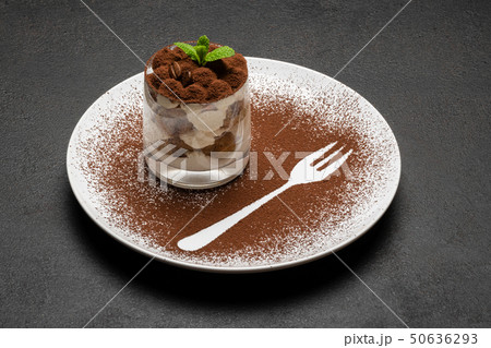 Classic tiramisu dessert in a glass on plate with fork silhouette on dark concrete background Classic tiramisu dessert in a glass on plate with fork silhouette on dark concrete background 50636293