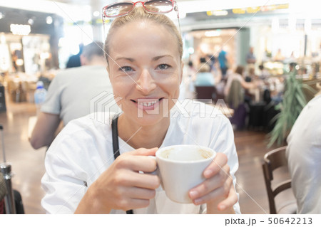 Portrait of a casual young blond woman having a cup of coffee, sitting in cafe indoors of an airport Portrait of a casual young blond woman having a cup of coffee, sitting in cafe indoors of an airport 50642213