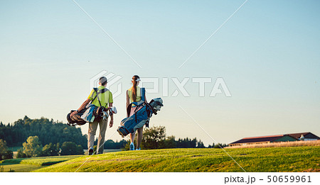 Happy couple carrying stand bags towards the golf course in a sunny day Happy couple carrying stand bags towards the golf course in a sunny day 50659961