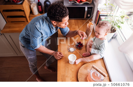 A top view of father and a small son eating fruit and yoghurt indoors at home. A top view of father and a small son eating fruit and yoghurt indoors at home. 50661076