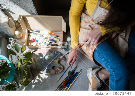Young beautiful lady artist in apron with paint stains sitting on the floor in her studio 50673447