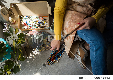 Young beautiful lady artist in apron with paint stains sitting on the floor in her studio 50673448