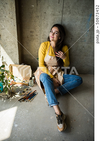 Young beautiful lady artist in apron with paint stains sitting on the floor in her studio 50673452