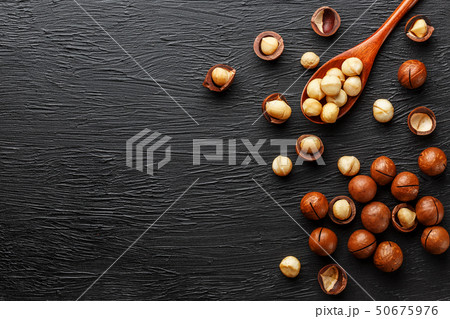 Shelled macadamia nut and peeled macadamia nut on a black textural background in a wooden spoon Shelled macadamia nut and peeled macadamia nut on a black textural background in a wooden spoon 50675976