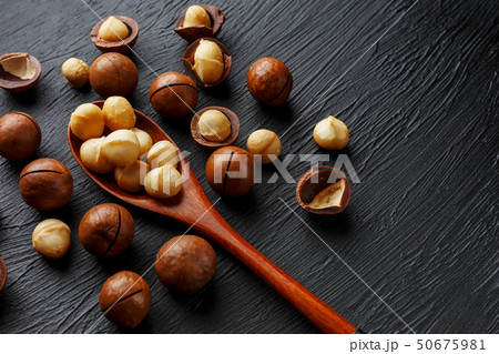 Shelled macadamia nut and peeled macadamia nut on a black textural background in a wooden spoon Shelled macadamia nut and peeled macadamia nut on a black textural background in a wooden spoon 50675981
