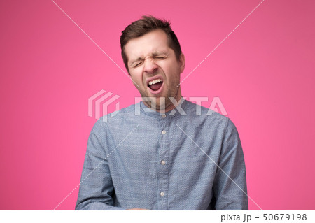 Tired man feels sleepy, yawns as feels tired, opens mouth widely, poses over pink background. Tired man feels sleepy, yawns as feels tired, opens mouth widely, poses over pink background. 50679198