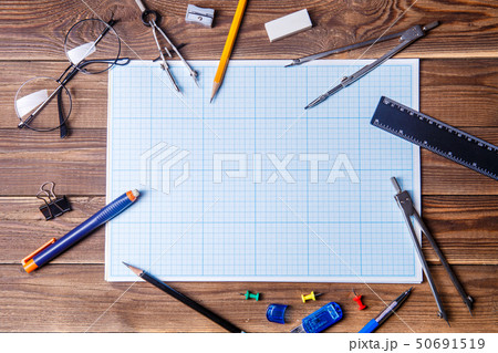 Graph paper with copyspace and student material on wooden table. Graph paper with copyspace and student material on wooden table. 50691519