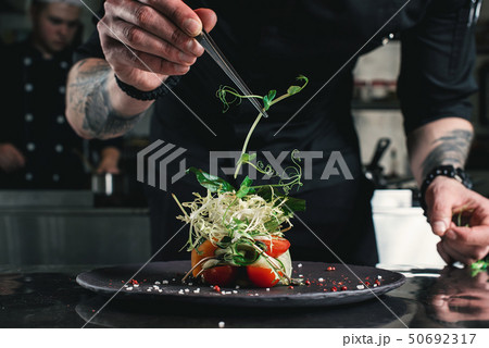 Chef finishing healthy salad on a black plate with tweezers. almost ready to serve it on a table 50692317