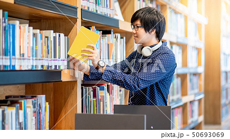 Asian man pulling book from bookshelf Asian man pulling book from bookshelf 50693069