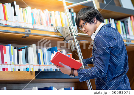 Asian guy choosing book from bookshelf in library Asian guy choosing book from bookshelf in library 50693075