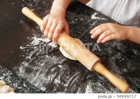 hands of small child palms rolling dough on brown table with rolling pin, view from above diagonally 50699717