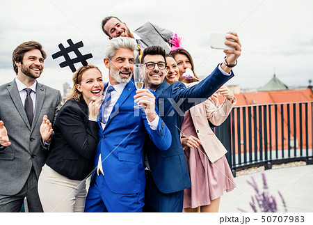 A group of joyful businesspeople outdoors on roof terrace in city, taking selfie on party. 50707983