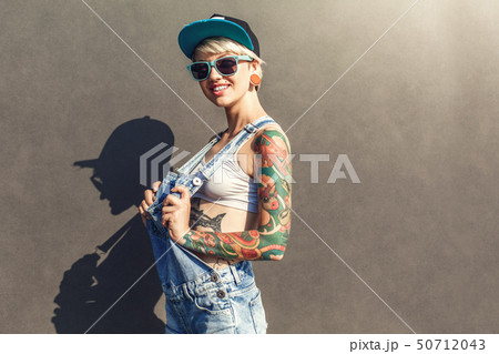 Freestyle. Alternative girl in cap ans sunglasses standing isolated on grey on the city street 50712043