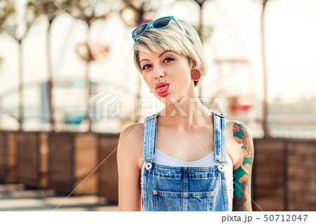 Summertime. Alternative girl in sunglasses up on head standing on the city street showing tongue to 50712047