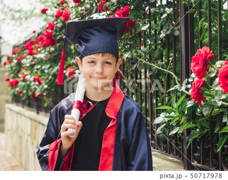 Happy caucasian child in graduation gown with diploma standing near stone fence full of wild roses Happy caucasian child in graduation gown with diploma standing near stone fence full of wild roses 50717978