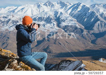 Portrait of a bearded traveler photographer in sunglasses and a cap sits on a rock with mirror 50720357