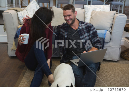 Couple using laptop with their pet dog in living room Couple using laptop with their pet dog in living room 50725670