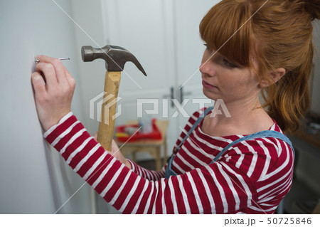 Female carpenter hammering nail on wall Female carpenter hammering nail on wall 50725846