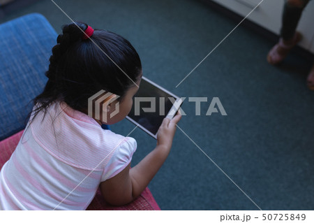 Schoolgirl studying on digital tablet while lying on the couch in school library Schoolgirl studying on digital tablet while lying on the couch in school library 50725849