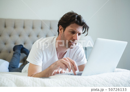 Man using laptop in bedroom 50726133