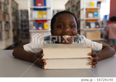 Happy schoolboy leaning his face on books and looking at camera on table 50726140