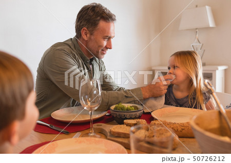 Father wiping daughters mouth with a napkin on dining table 50726212