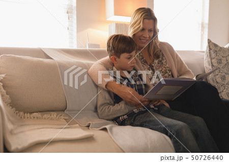 Mother with her son reading story book in living room 50726440