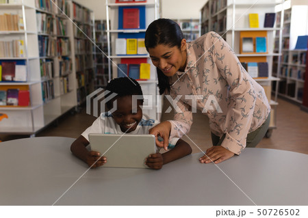 Female teacher teaching schoolboy on digital tablet at table in school library 50726502