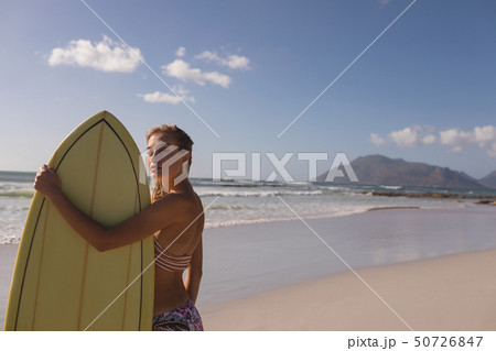 Female surfer standing with surfboard at beach 50726847