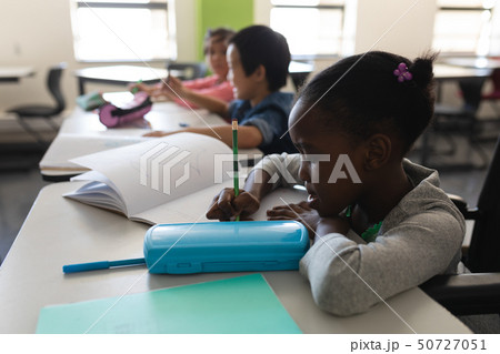 Side view of disable black schoolgirl studying and sitting at desk in classroom Side view of disable black schoolgirl studying and sitting at desk in classroom 50727051