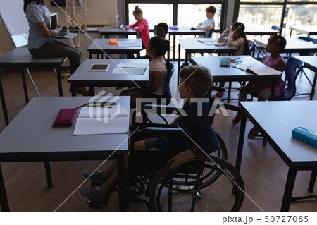 Disable schoolboy with classmates studying and sitting at desk in classroom Disable schoolboy with classmates studying and sitting at desk in classroom 50727085