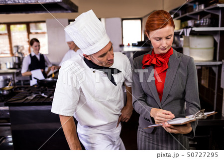 Female manager and male chef writing on clipboard in kitchen 50727295