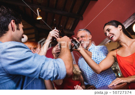Friends toasting beer bottle in nightclub 50727374