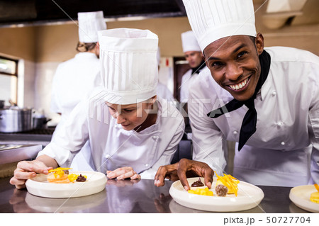 Male and female chefs garnishing delicious desserts in a plate Male and female chefs garnishing delicious desserts in a plate 50727704