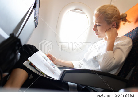 Woman reading in flight magazine on airplane. Female traveler reading seated in passanger cabin. Sun 50733462