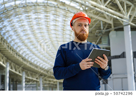 A man in a helmet in a large space with a tablet A man in a helmet in a large space with a tablet 50742296