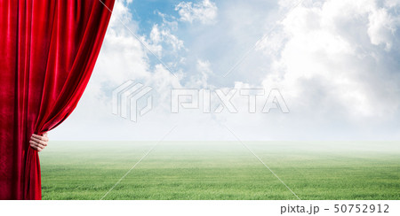Green meadow behind red curtain and hand holding it Green meadow behind red curtain and hand holding it 50752912