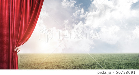 Green meadow behind red curtain and hand holding it Green meadow behind red curtain and hand holding it 50753691
