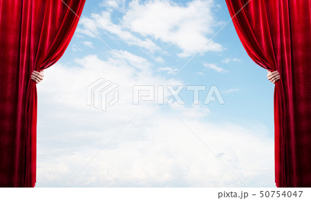Cloudy landscape behind red curtain and hand holding it Cloudy landscape behind red curtain and hand holding it 50754047