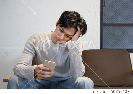 スマートフォンを手に考え込む男性 50756583