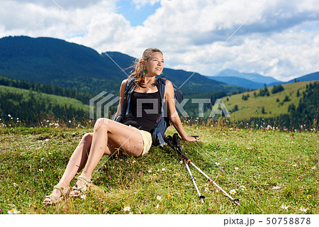 Woman hiker hiking on grassy hill, wearing backpack, using trekking sticks in the mountains Woman hiker hiking on grassy hill, wearing backpack, using trekking sticks in the mountains 50758878
