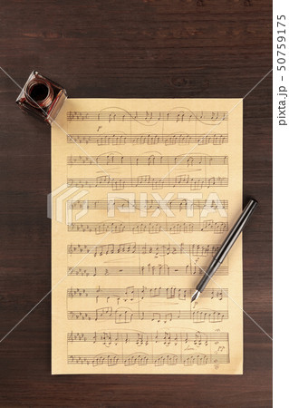 A piece of sheet music, shot from above on a dark rustic wooden background with a nib pen and an ink 50759175