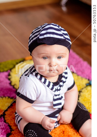 A pretty baby in a striped shirt and hats seated on the mat in the room A pretty baby in a striped shirt and hats seated on the mat in the room 50763553